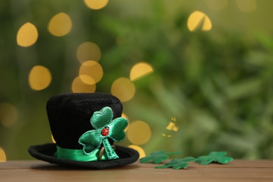 Photo of Leprechaun hat and clover leaves on wooden table against blurred lights, space for text. St Patrick's Day celebration