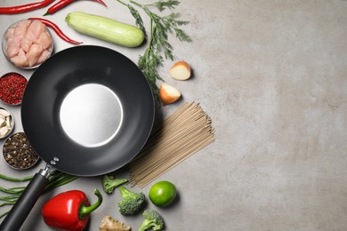 Photo of Empty iron wok surrounded by raw ingredients on grey table, flat lay. Space for text