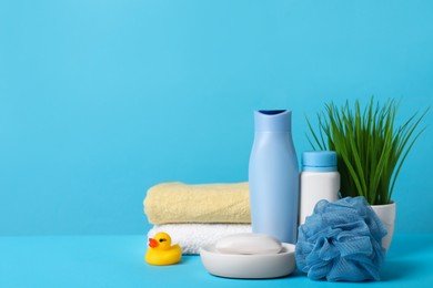 Photo of Baby cosmetic products, bath duck, sponge and towels on light blue background. Space for text