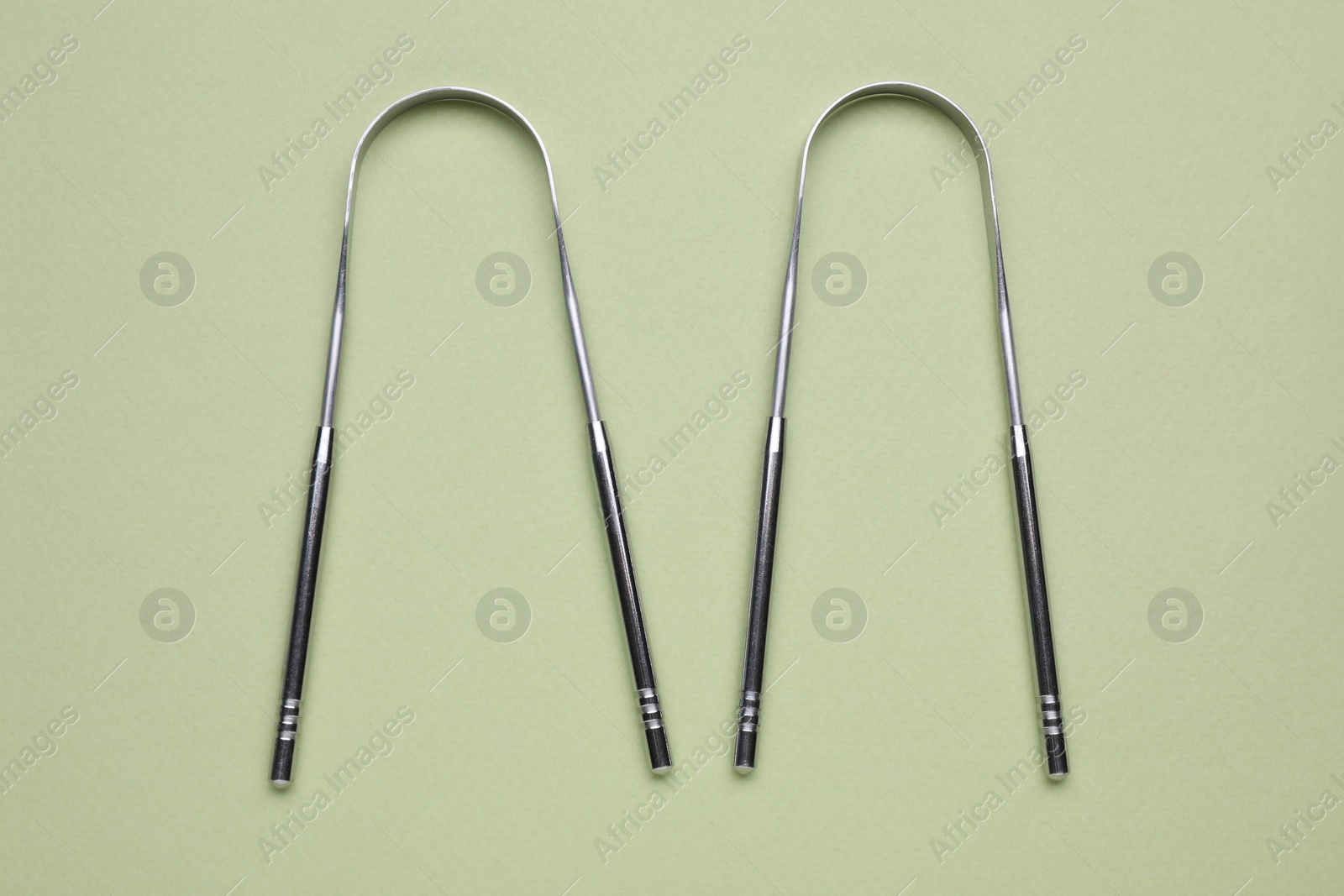 Photo of Metal tongue cleaners on olive background, flat lay