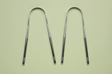 Photo of Metal tongue cleaners on olive background, flat lay