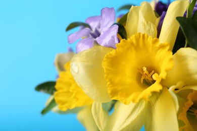 Photo of Bouquet of beautiful yellow daffodils and periwinkle flowers on light blue background, closeup. Space for text