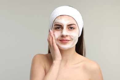 Photo of Young woman with headband washing her face on light grey background