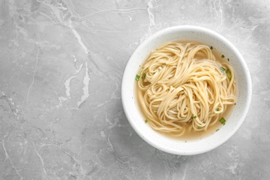 Bowl of tasty noodles with broth on table, top view. Space for text