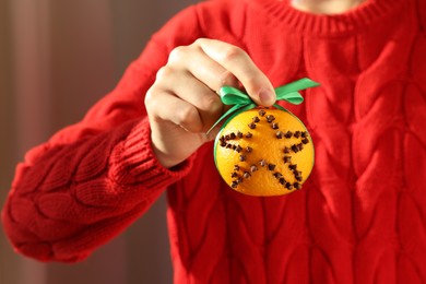 Photo of Woman holding pomander ball with green ribbon made of fresh tangerine and cloves on color background, closeup