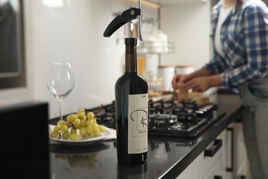 Photo of Wine bottle with corkscrew on black countertop, closeup. Woman in kitchen, selective focus