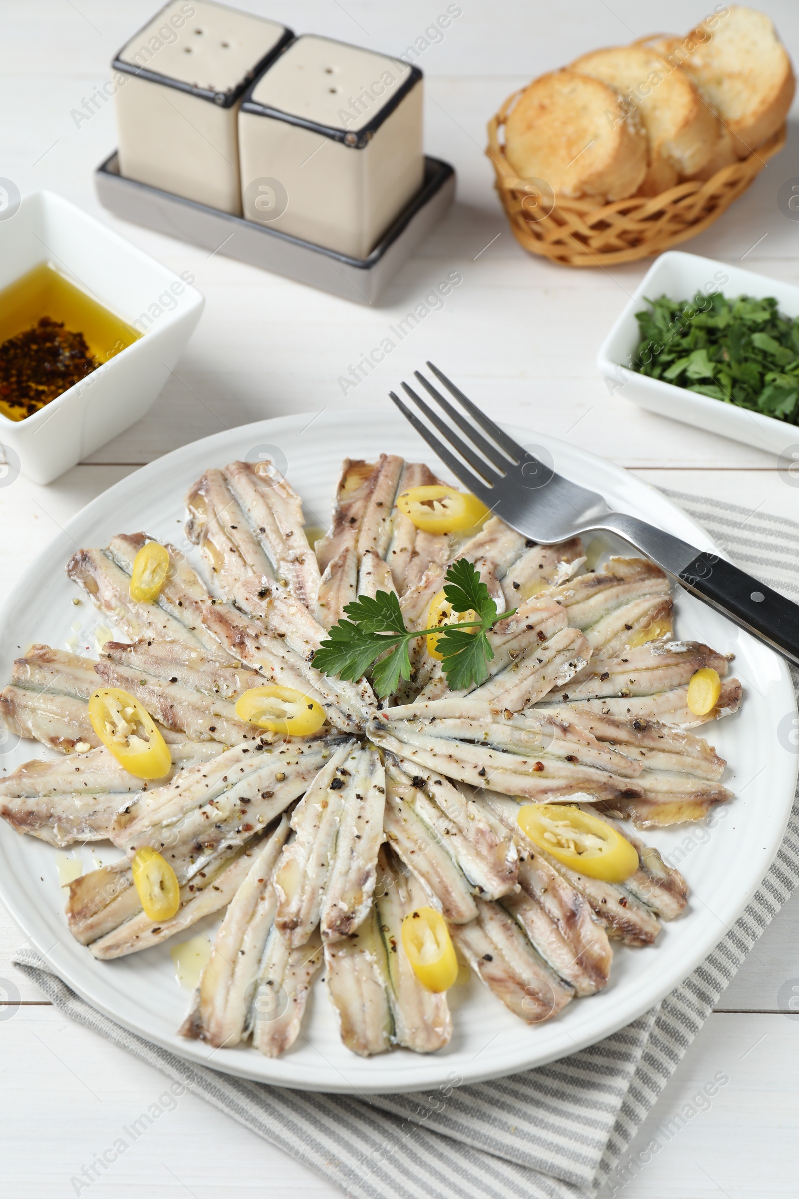 Photo of Tasty pickled anchovies served on white wooden table