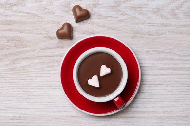 Cup of hot chocolate with heart shaped marshmallows and candies on white wooden table, flat lay