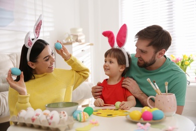 Photo of Happy family having fun while painting Easter eggs at table indoors