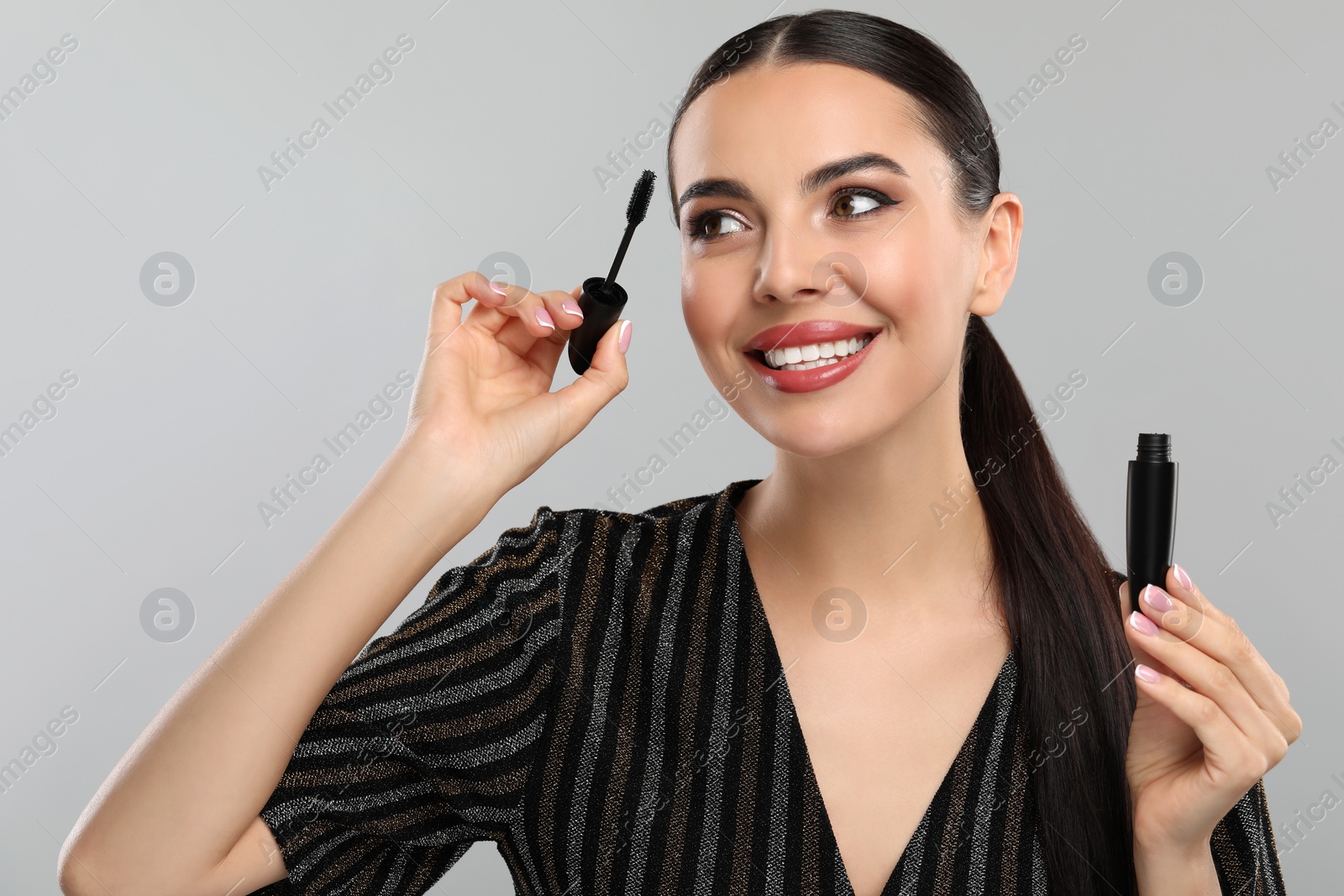 Photo of Everyday makeup. Beautiful woman applying mascara on light grey background