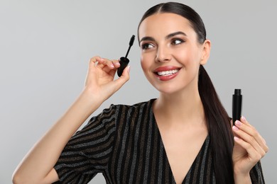 Everyday makeup. Beautiful woman applying mascara on light grey background