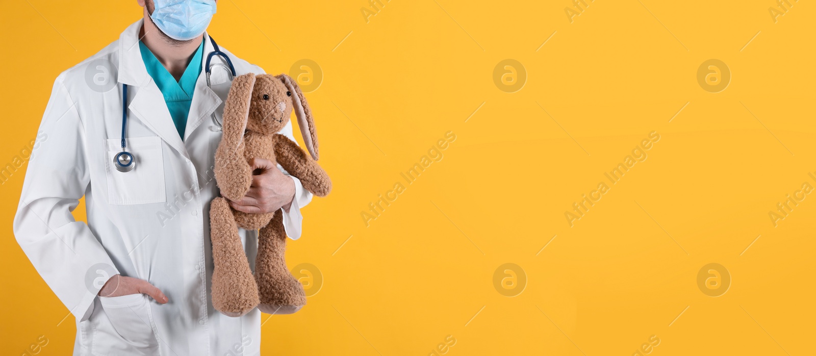 Photo of Pediatrician with toy bunny and stethoscope on yellow background, closeup. Space for text