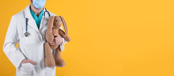 Pediatrician with toy bunny and stethoscope on yellow background, closeup. Space for text