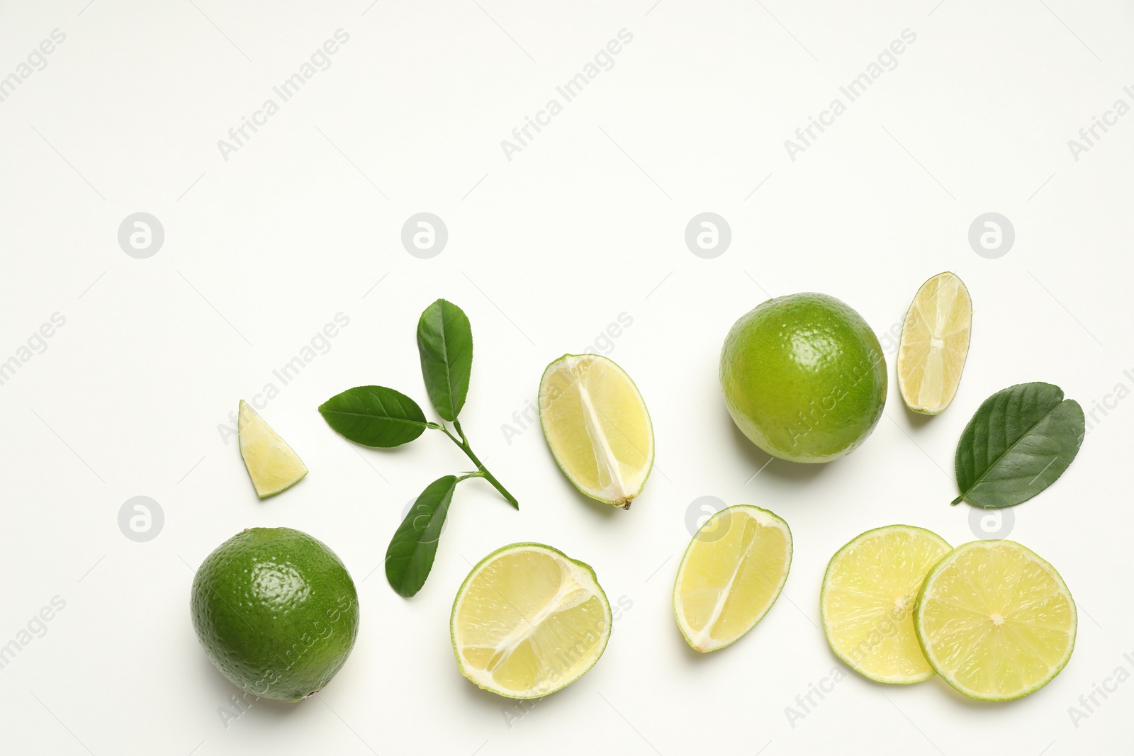 Photo of Whole and cut fresh ripe limes with green leaves on white background, flat lay