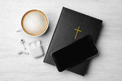 Photo of Bible, phone, cup of coffee and earphones on white wooden background, flat lay. Religious audiobook