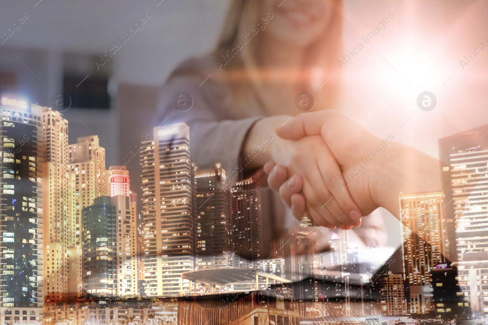 Image of Double exposure of night cityscape and business people shaking hands in office, closeup. Team work 
