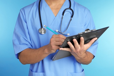 Male doctor with stethoscope and clipboard on color background, closeup. Medical objects