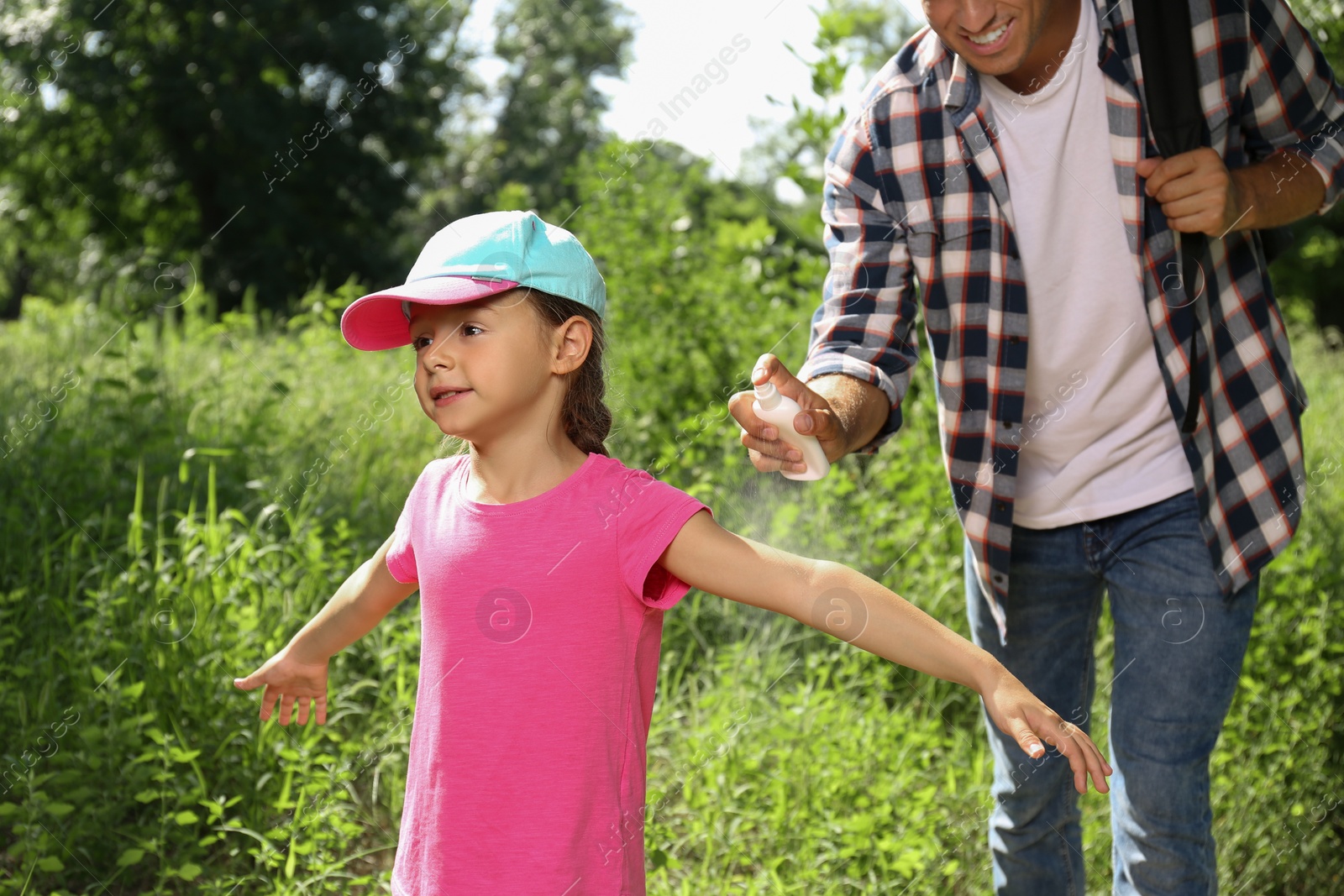 Photo of Father spraying tick repellent on his little daughter's arm during hike in nature