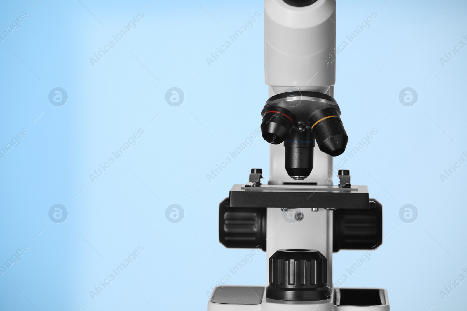 Photo of Modern microscope on light blue background, closeup. Space for text