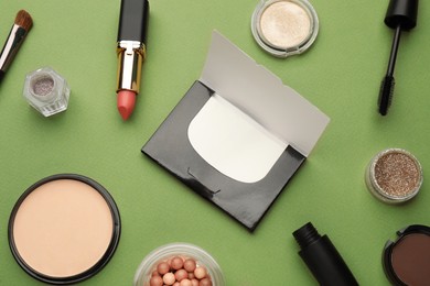 Photo of Flat lay composition with facial oil blotting tissues and makeup products on green background. Mattifying wipes
