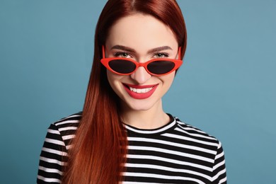 Happy woman with red dyed hair and sunglasses on light blue background