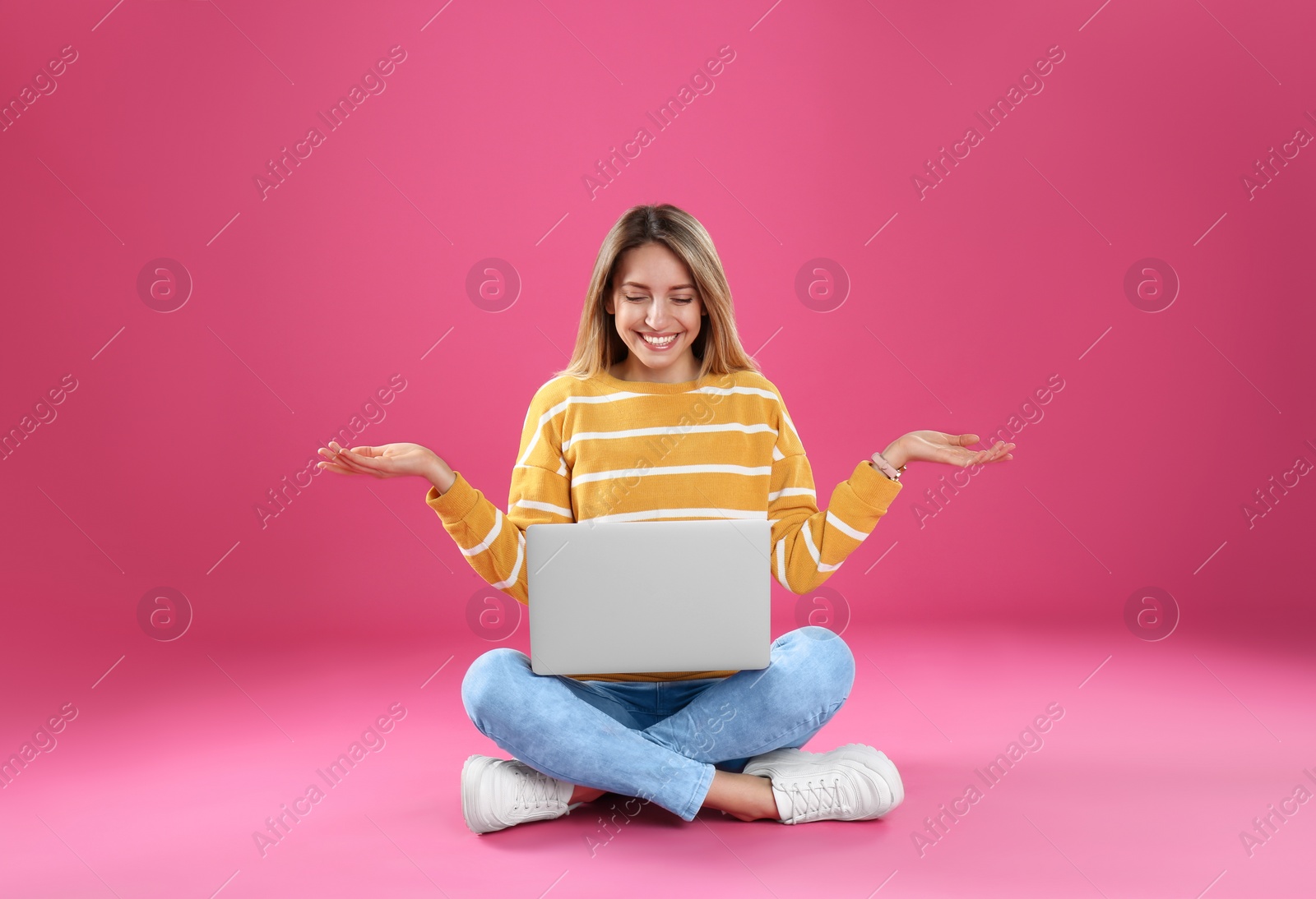 Photo of Young woman in casual outfit with laptop sitting on color background