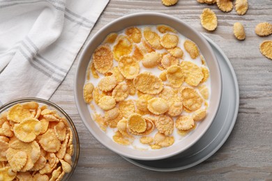 Tasty cornflakes with milk in bowl on wooden table, flat lay