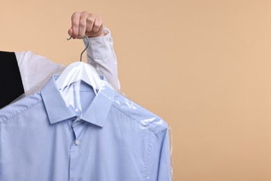 Photo of Dry-cleaning service. Woman holding shirt in plastic bag on beige background, closeup. Space for text