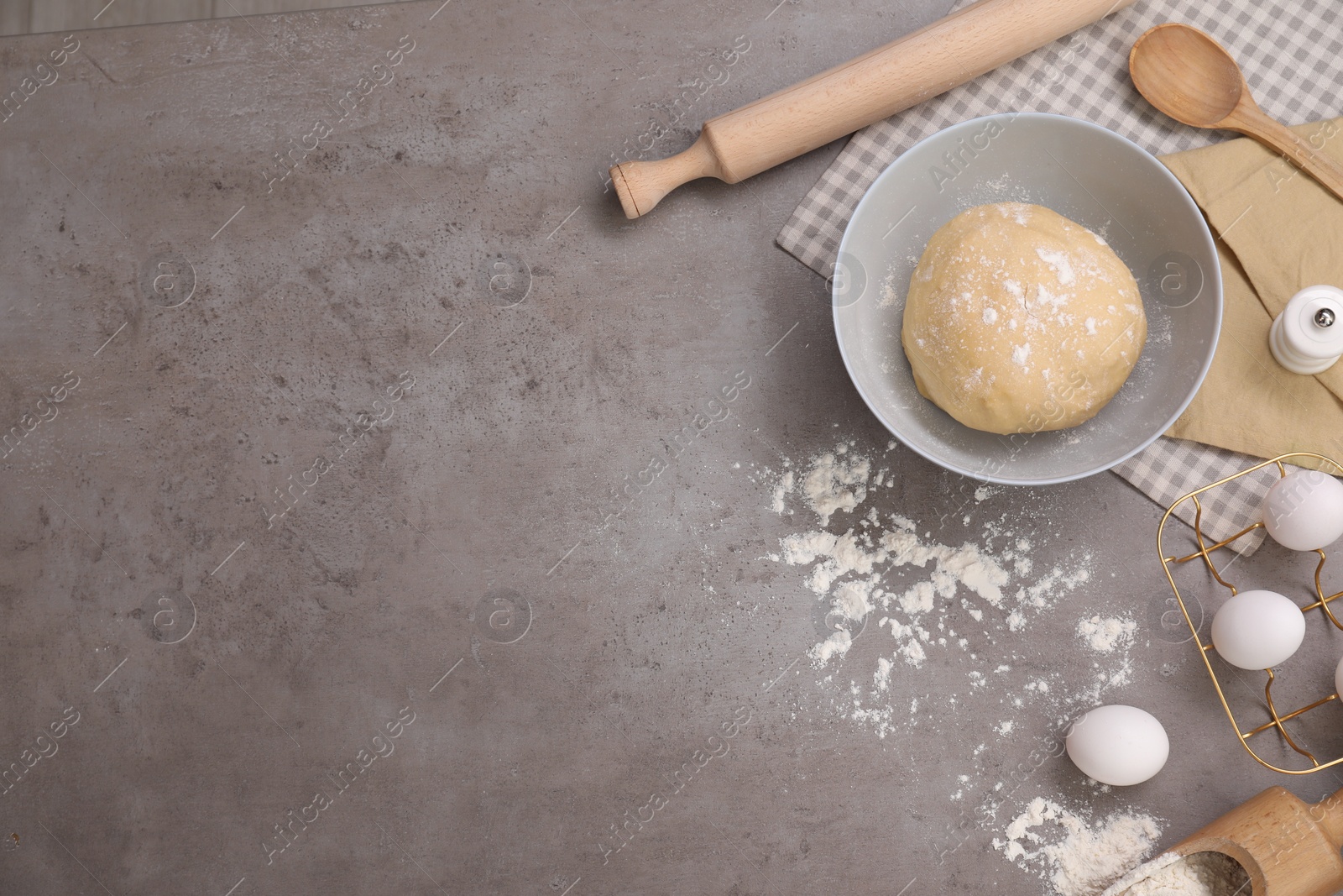 Photo of Making tasty baklava. Raw dough, eggs, flour and rolling pin on grey table, flat lay with space for text
