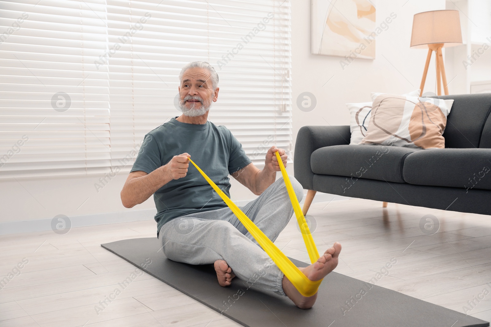 Photo of Senior man doing exercise with fitness elastic band on mat at home