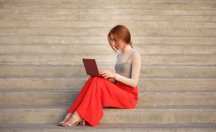 Photo of Beautiful young woman with laptop sitting on stairs outdoors