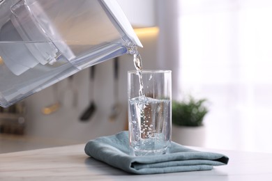 Photo of Pouring water from filter jug into glass in kitchen, closeup