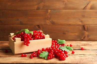 Photo of Delicious red currants and leaves on wooden table. Space for text