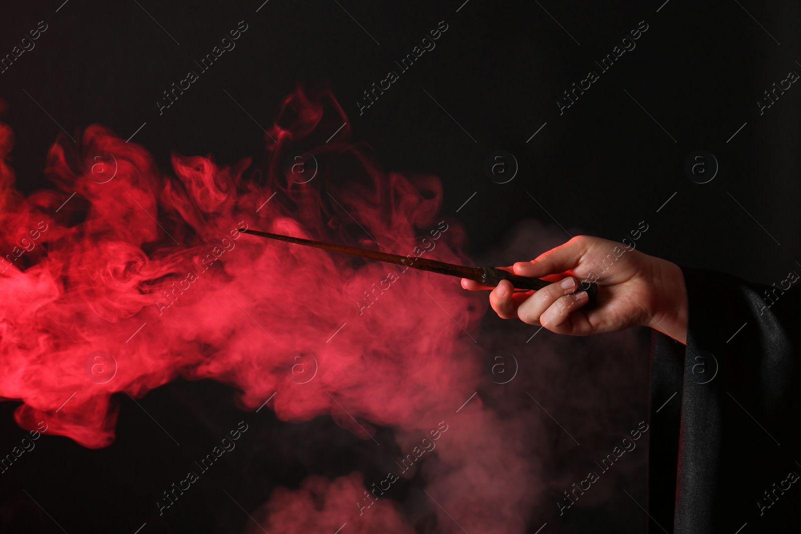 Photo of Magician holding wand in smoke on dark background, closeup