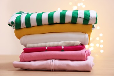Photo of Stack of folded clothes on wooden table against beige background with blurred lights
