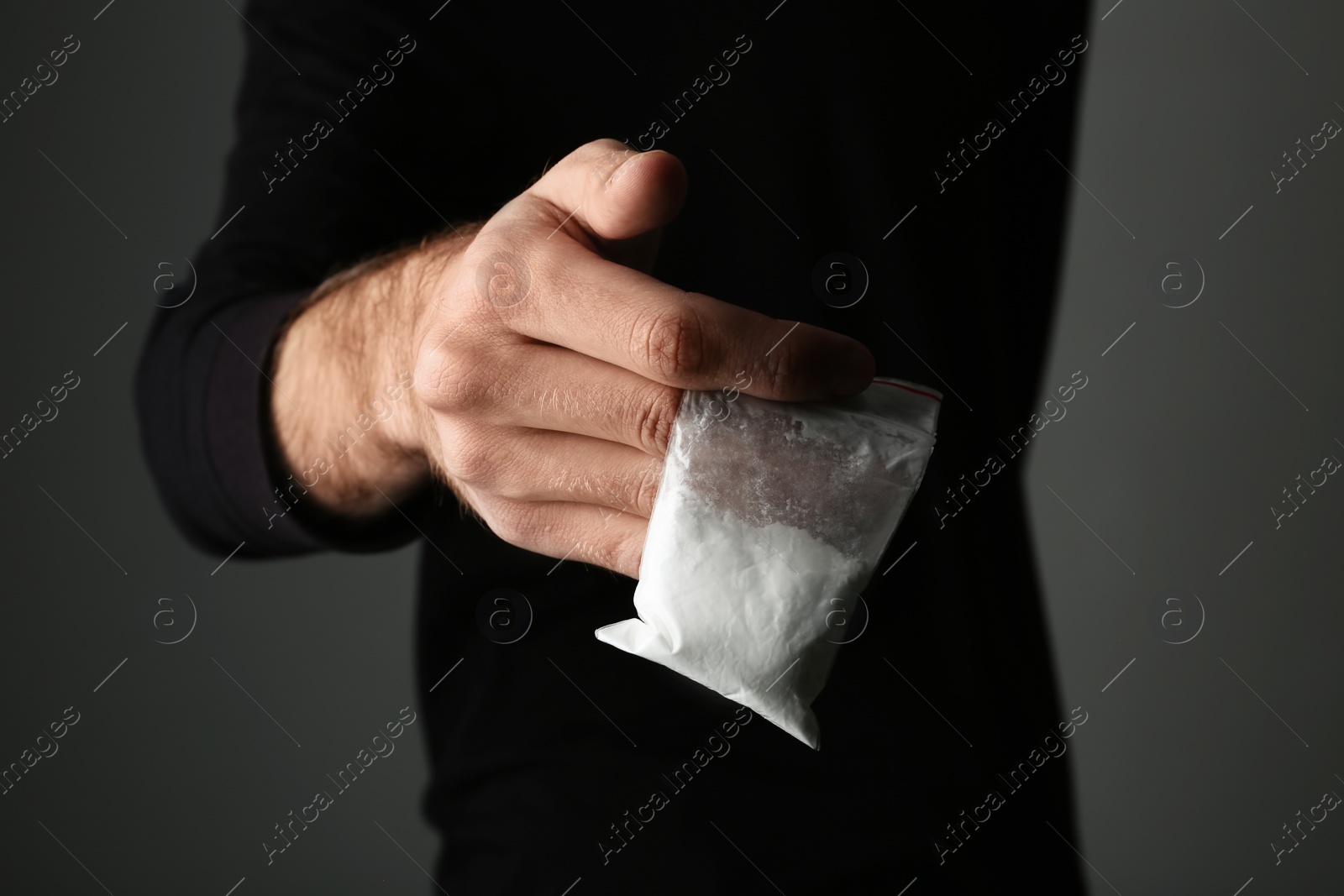 Photo of Drug dealer holding bag with cocaine on dark background, closeup