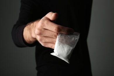 Photo of Drug dealer holding bag with cocaine on dark background, closeup