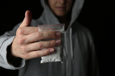 Photo of Drug dealer holding bag with cocaine on black background, closeup