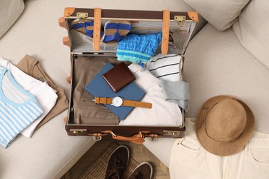Photo of Open suitcase with different men clothes and accessories on sofa, top view