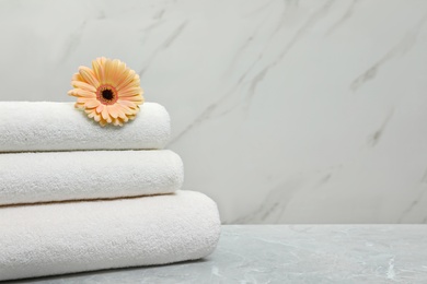 Photo of Stack of fresh towels with flower on grey table against light background. Space for text