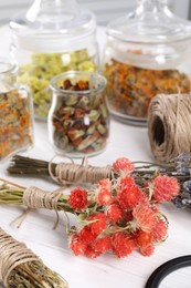 Bunches of dry flowers, different medicinal herbs and spool on white wooden table