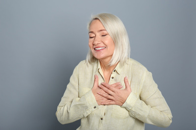 Happy woman holding hands near heart on grey background