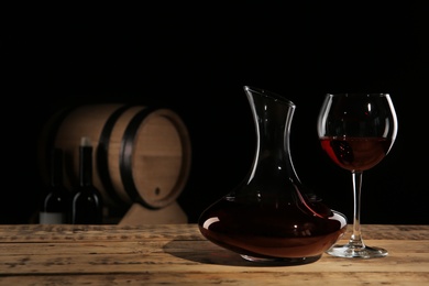 Photo of Elegant decanter and glass with red wine on table against dark background