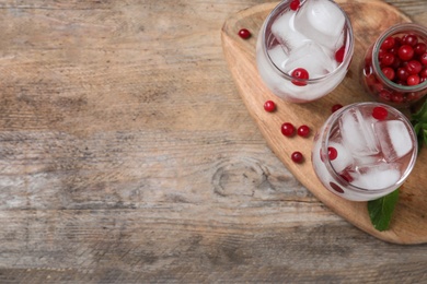 Photo of Glasses of cocktail with vodka, ice and cranberry on wooden table, top view. Space for text