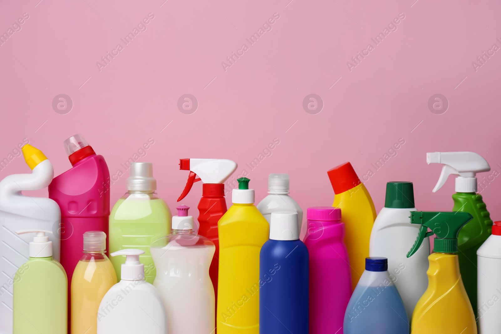 Photo of Many bottles of different detergents on pink background. Cleaning supplies