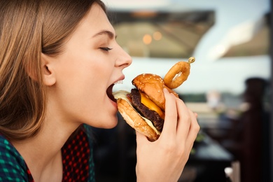 Photo of Young woman eating burger in street cafe