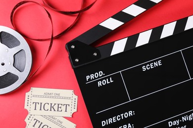 Photo of Clapperboard, movie tickets and film reel on red background, flat lay