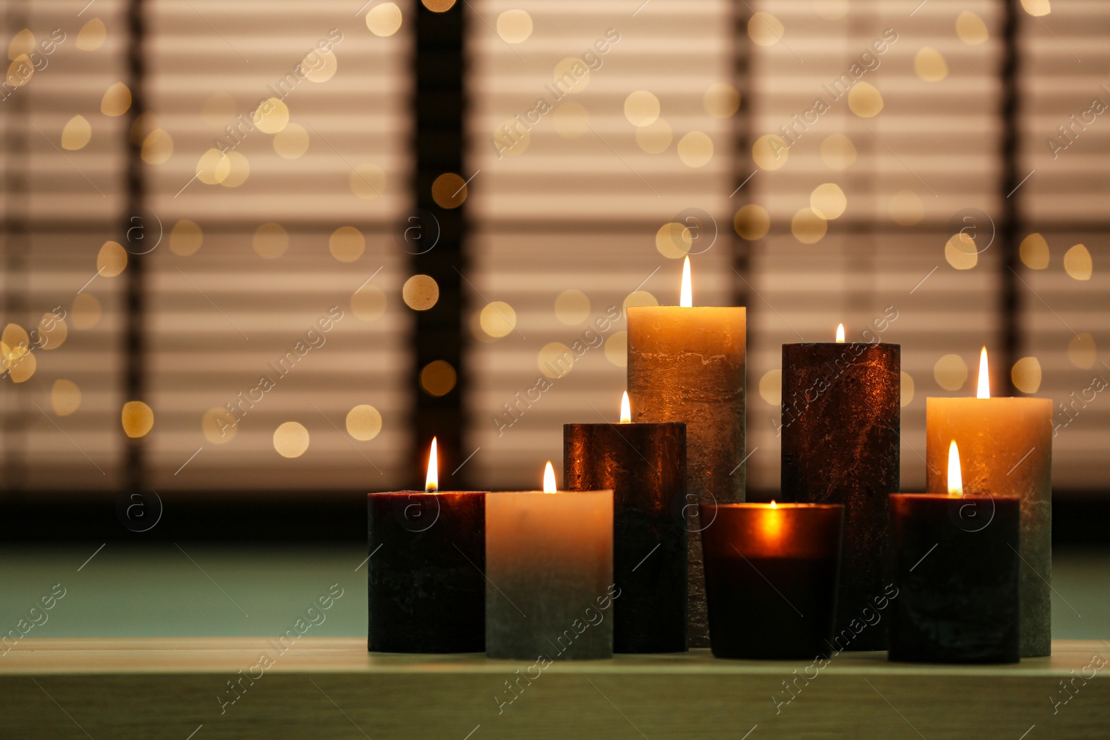 Photo of Beautiful burning candles on wooden table against festive lights. Space for text