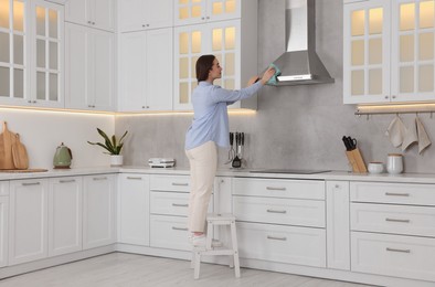 Photo of Woman on ladder wiping kitchen hood at home