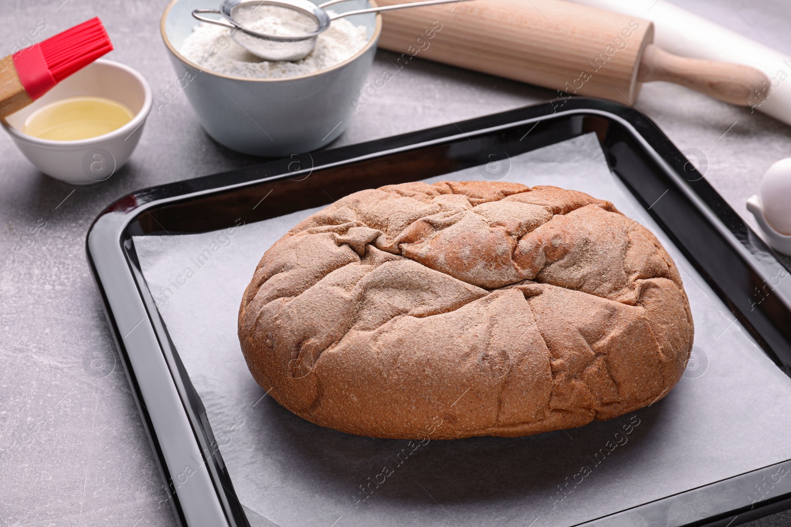 Photo of Baking pan with tasty homemade bread and parchment paper on light grey table